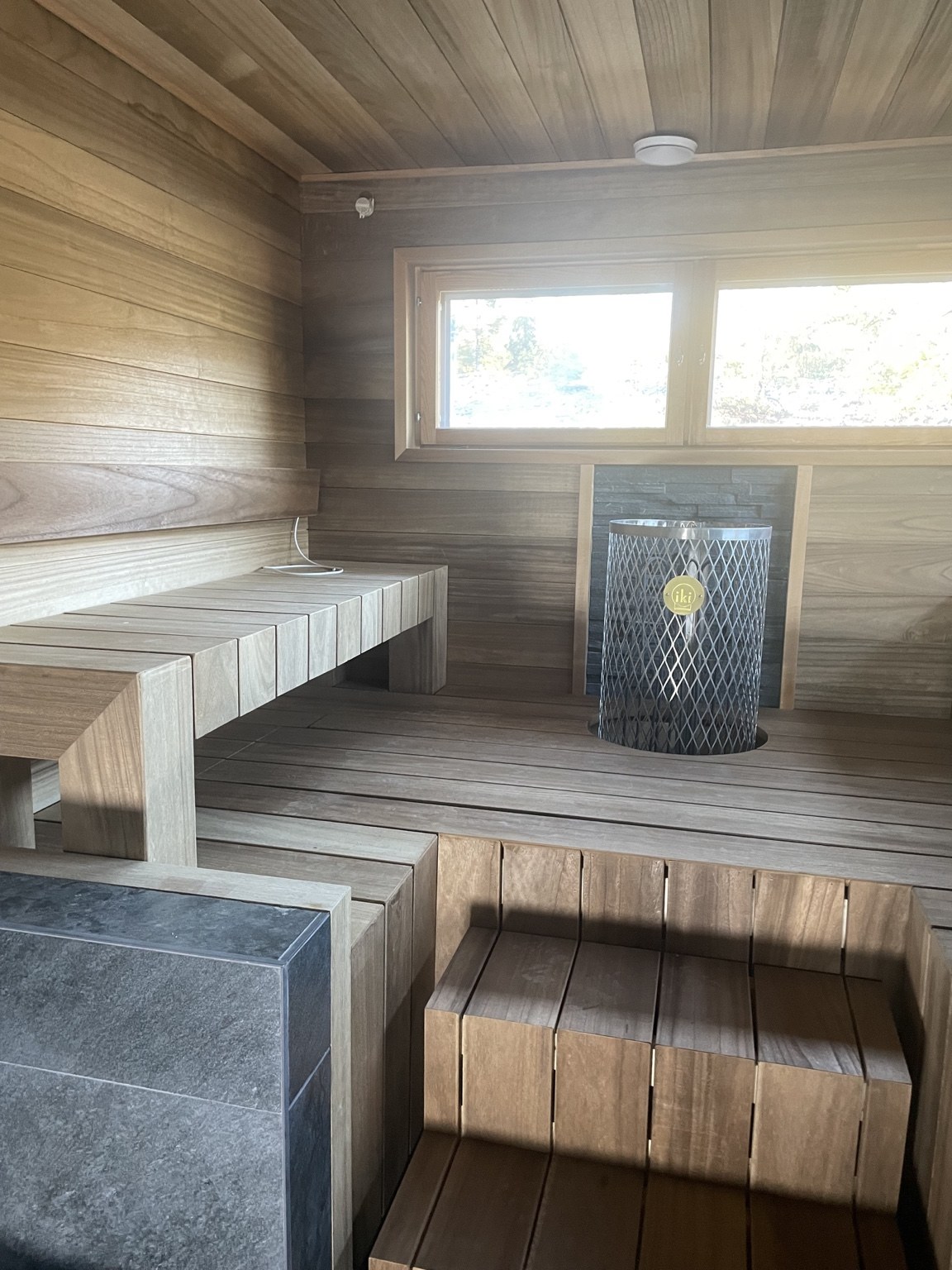 Vaalea sauna, leveät puulauteet ja tumma kiuas